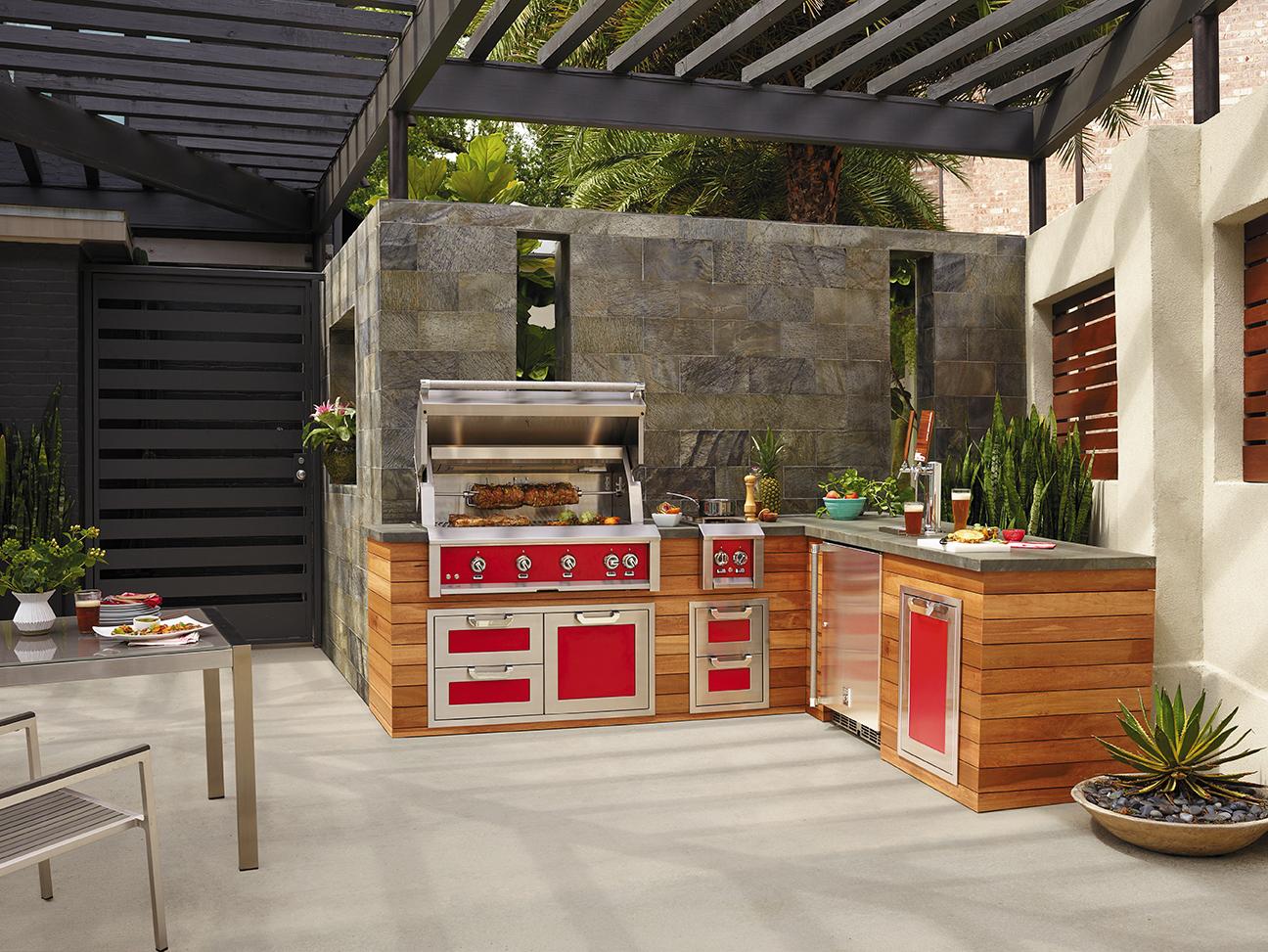 后院露台厨房，有红色电器和石头台面，正在准备食物和烤肉