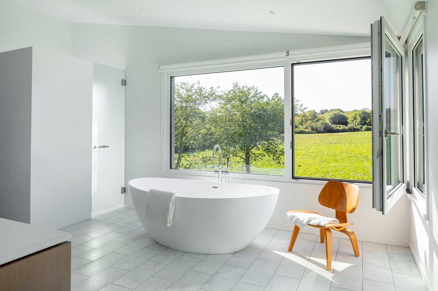 large white tub with a chair next to it and open window